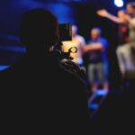 A cameraman films a live concert performance, capturing the dynamic stage action.